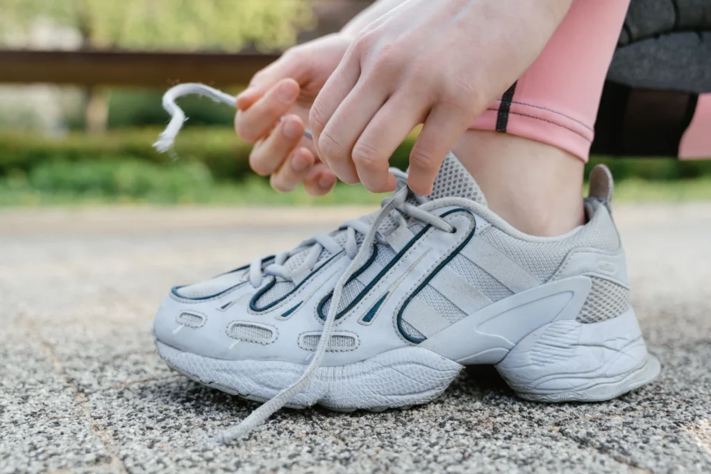 Zbliżenie na kobietę zawiązującą sznurowadła w białych sneakersach podczas ćwiczeń na świeżym powietrzu.
